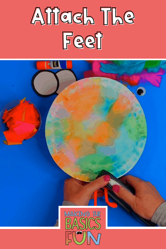 pipe cleaner bird feet being stapled between two colorful paper plates